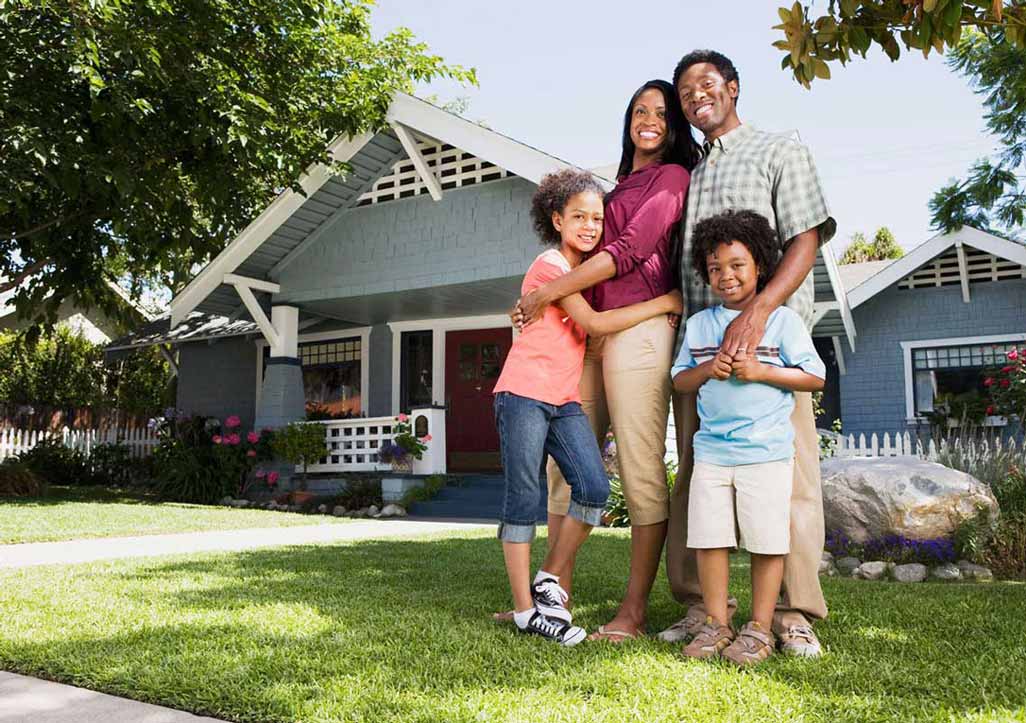 A family standiing in front of a grey house on a sunny day